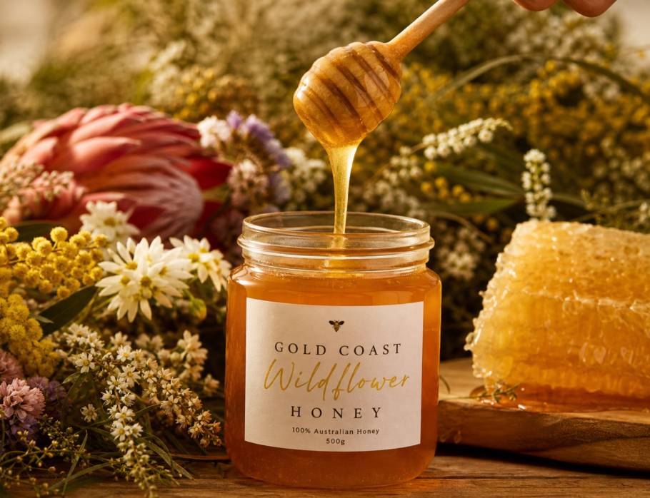 Golden raw honey being poured from a wooden dipper into a glass jar with native Australian flowers