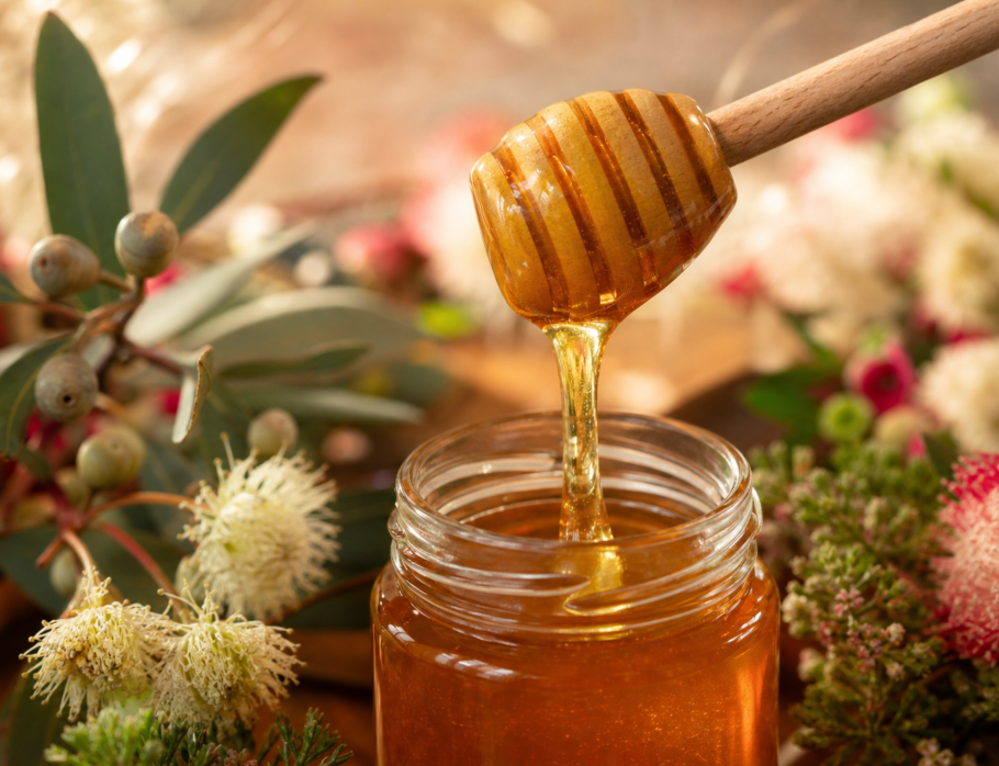 Brisbane honey - golden raw honey being poured from a wooden dipper into a glass jar with native Australian flora