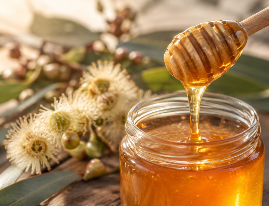 Raw honey dripping from a wooden dipper into a glass jar beside eucalyptus blossom, Gold Coast honey