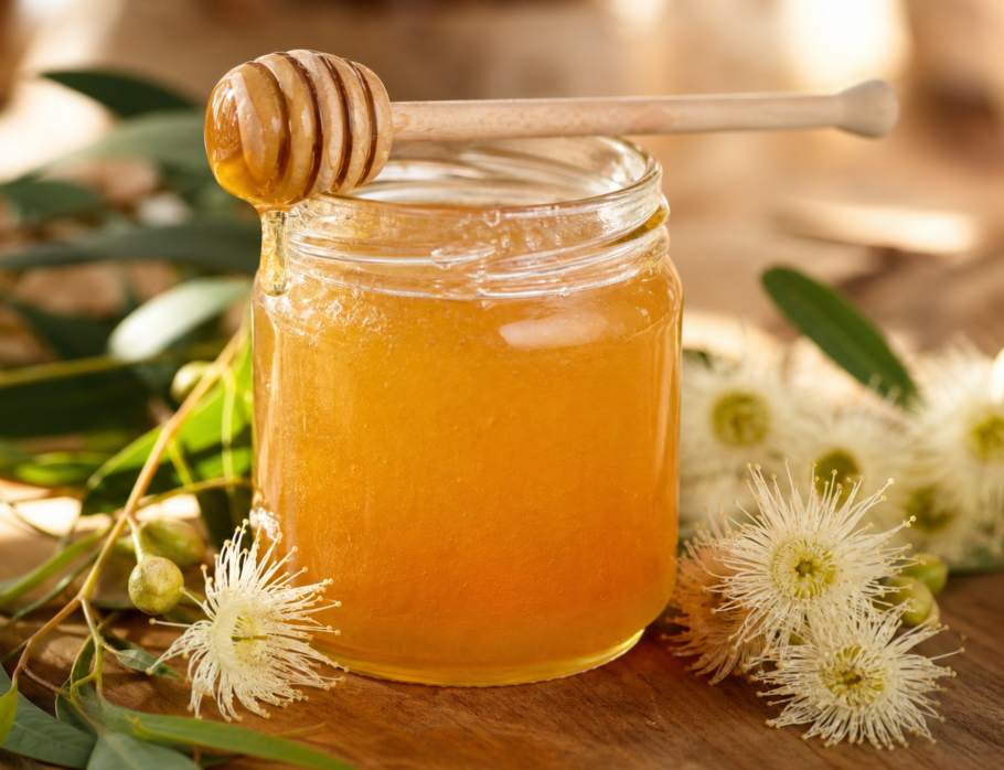 Jar of unfiltered unheated raw honey with honey dipper and Queensland eucalyptus blossoms