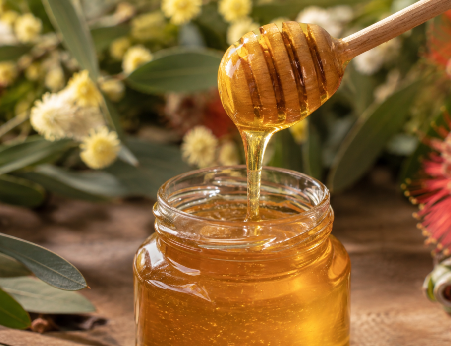 Raw honey dripping from a wooden dipper into a glass jar with Australian native wildflowers, showing the health benefits of raw honey