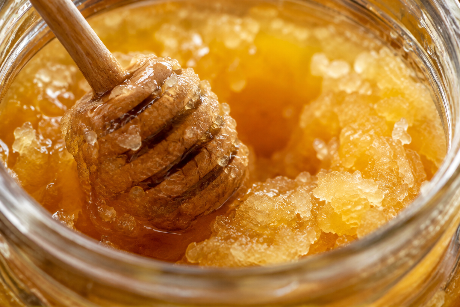 Close-up of raw honey crystals forming in a glass jar with a wooden honey dipper