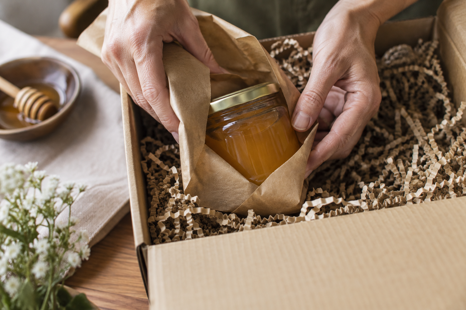 Hands wrapping a glass jar of raw honey in kraft paper for posting